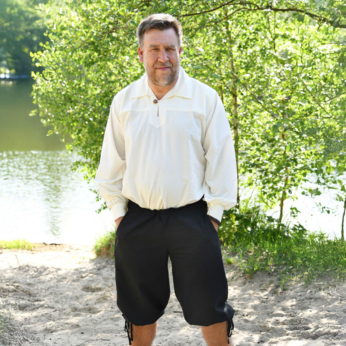Mann trägt schwarze Mittelalterhose Knickerbocker Jonte aus Baumwolle mit Bindung am Knie von mareg.net am Seeufer